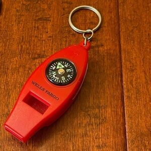 Red multi-functional keychain with a compass and a whistle.